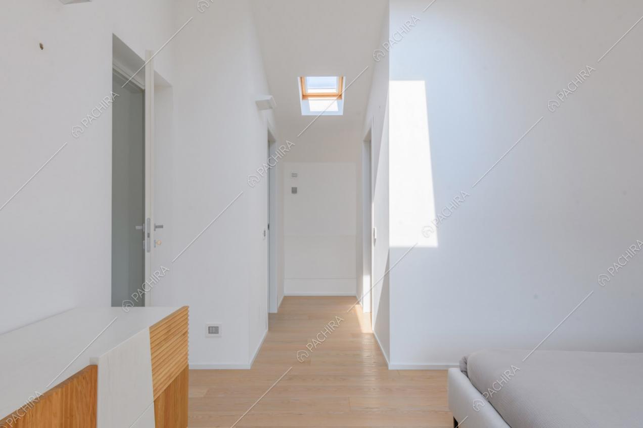 Grande camera da letto matrimoniale con lucernario, pareti bianche e pavimento in parquet