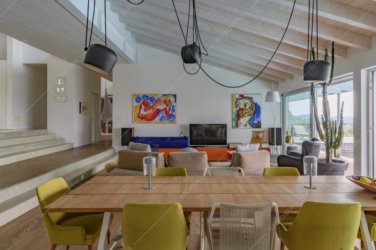 Tavolo da pranzo in legno nella sala con pareti bianche, soffitto in travi in legno a vista e ampie porte-finestre scorrevoli
