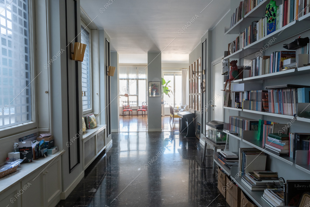 Corridoio con pavimento nero in piastrelle illuminato dalle ampie vetrate e vista sulla sala