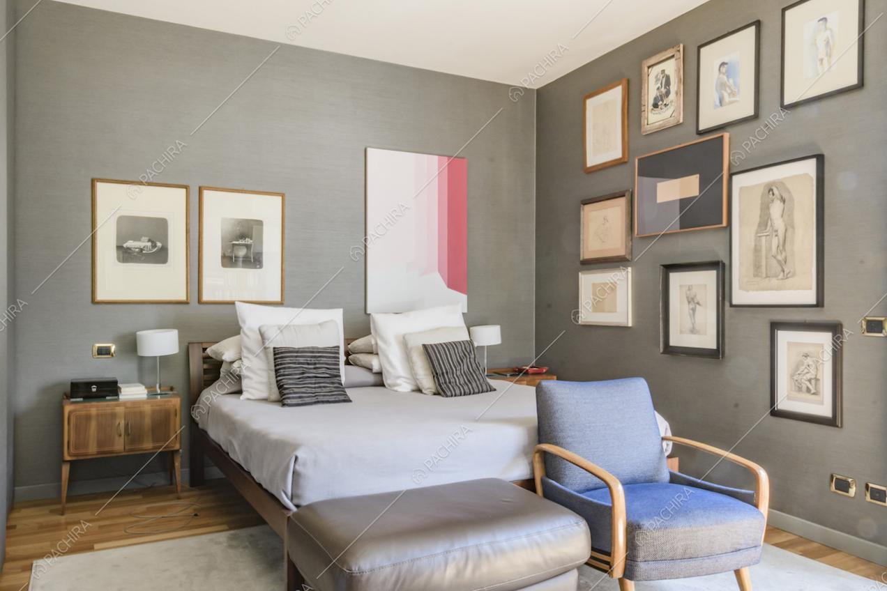 Camera matrimoniale con letto, poltroncina e pareti grigie con quadri