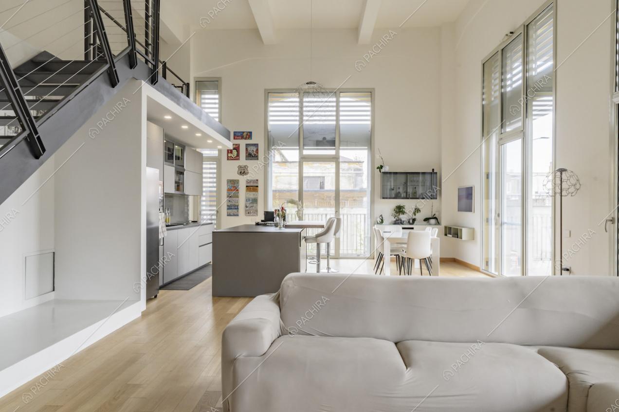 Salotto con pavimento in parquet, divano angolare e cucina a vista con isola