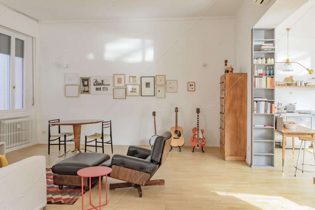 La zona living con tavolo in legno, pareti bianche e chitarre esposte