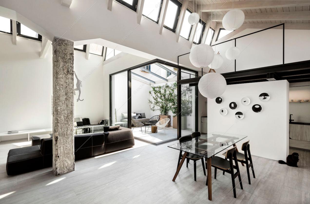 Sala con tavolo da pranzo con piano da lavoro in vetro, divano nero e giardino d'inverno