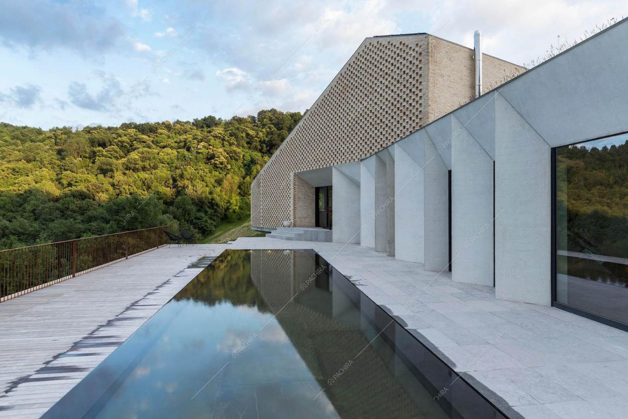 Piscina con fondo mobile sulla terrazza, grandi vetrate, esterni bianchi e in mattoni rossi a vista