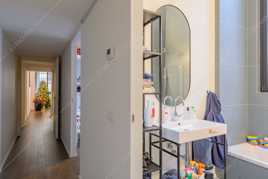 Dal corridoio con pareti bianche e pavimento in parquet vista sul bagno