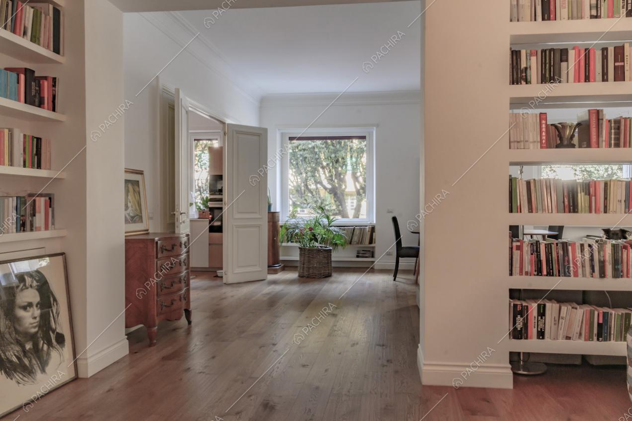 Dall'atrio con pavimento in parquet e libreria scorcio sulla cucina e su un'ampia vetrata della sala