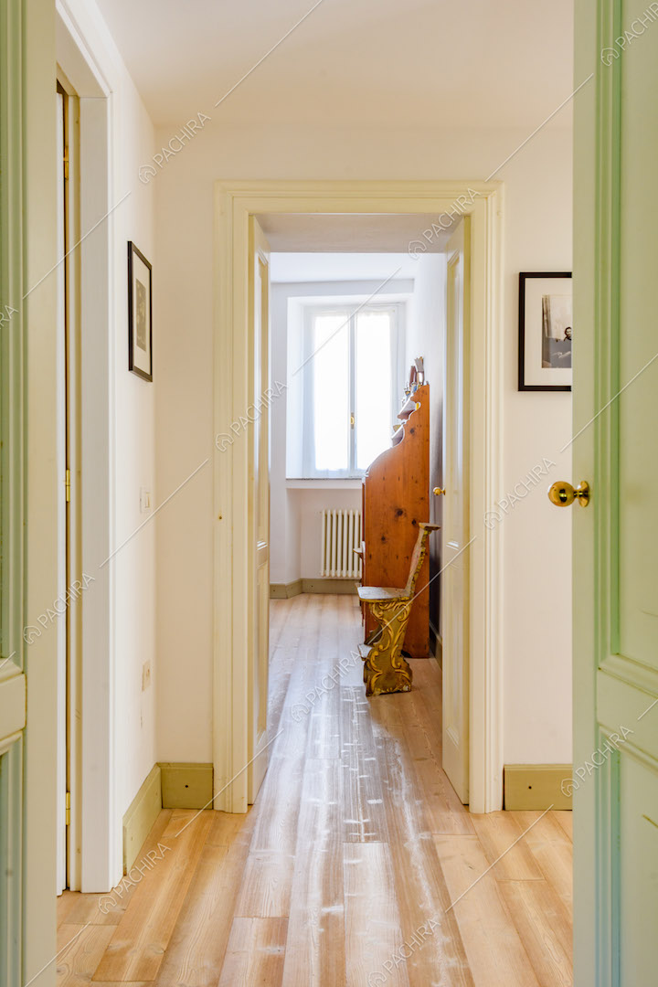 Corridoio con pareti bianche, porte verdi con boiserie e pavimento in parquet