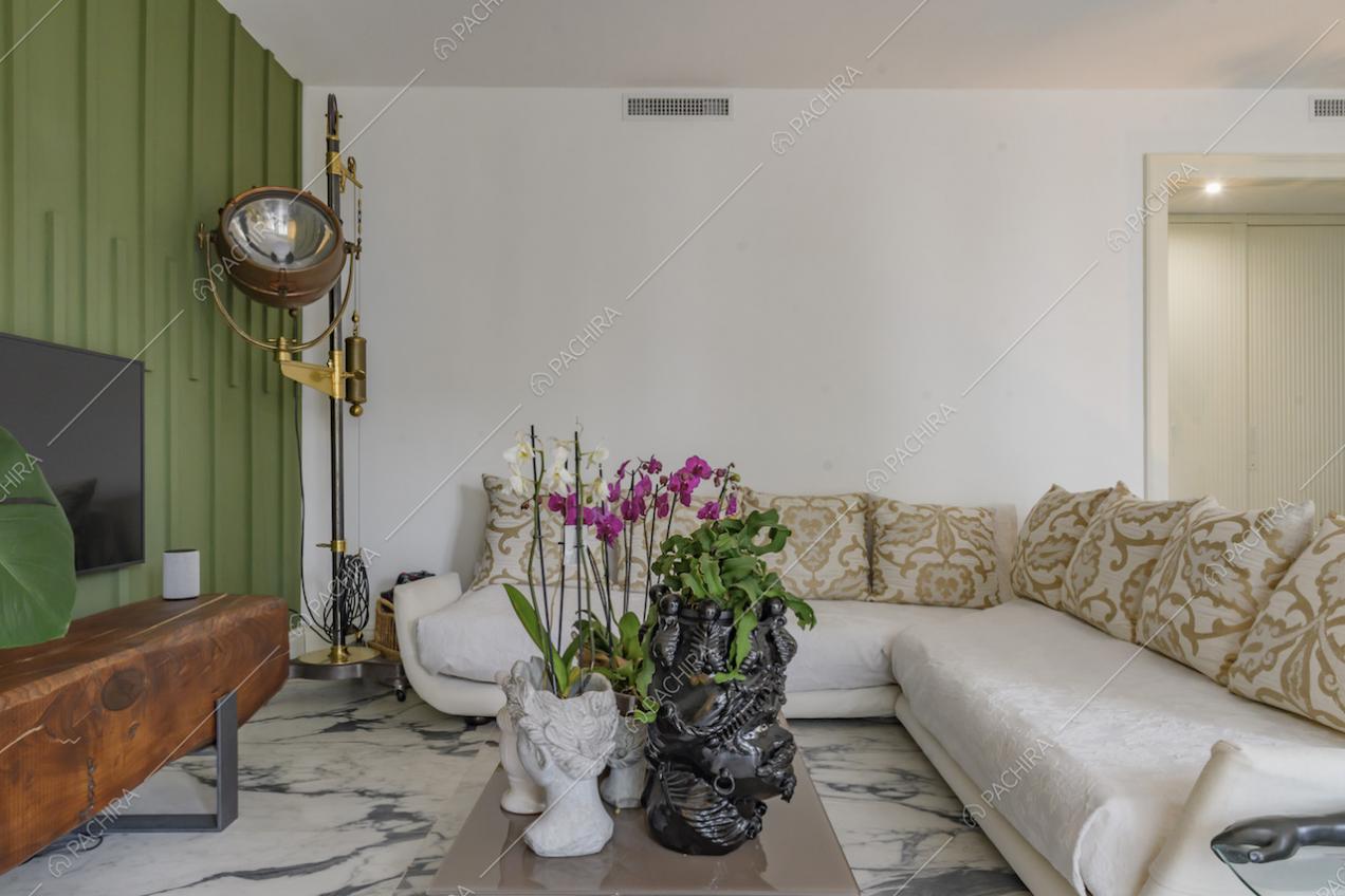 Salotto con parete verde con boiserie, divano bianco angolare e faro da set come lampada