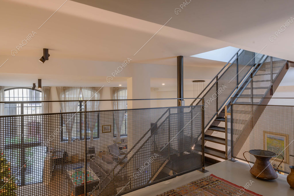 Dal soppalco con balaustra in metallo vista sulle scale e sulla zona living con alto soffitto