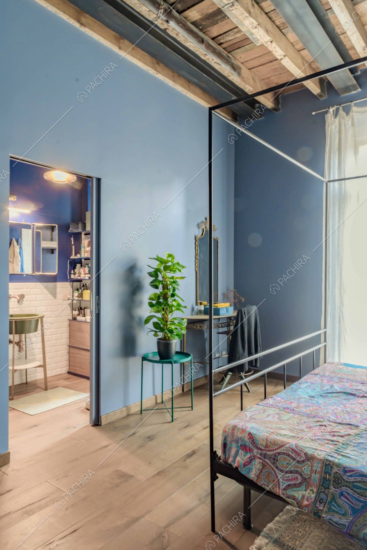 Camera da letto matrimoniale con pareti azzurre, soffitto con travi in legno a vista e bagno privato