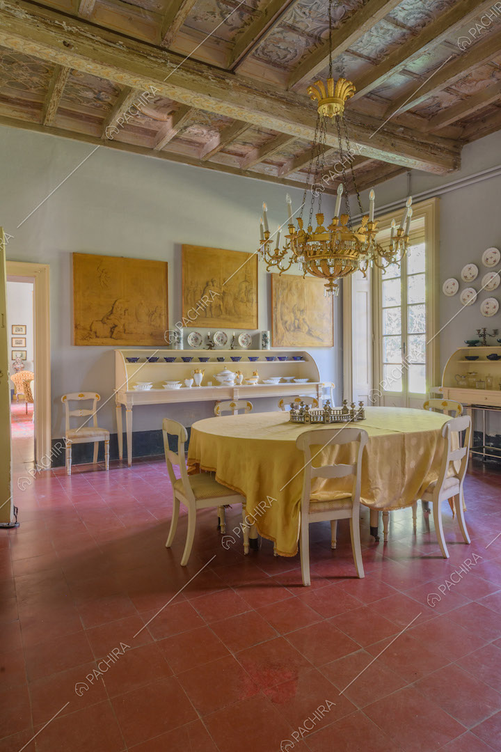 Grande sala da pranzo con pavimento in piastrelle rosse, soffitto a cassettoni e porta-finestra