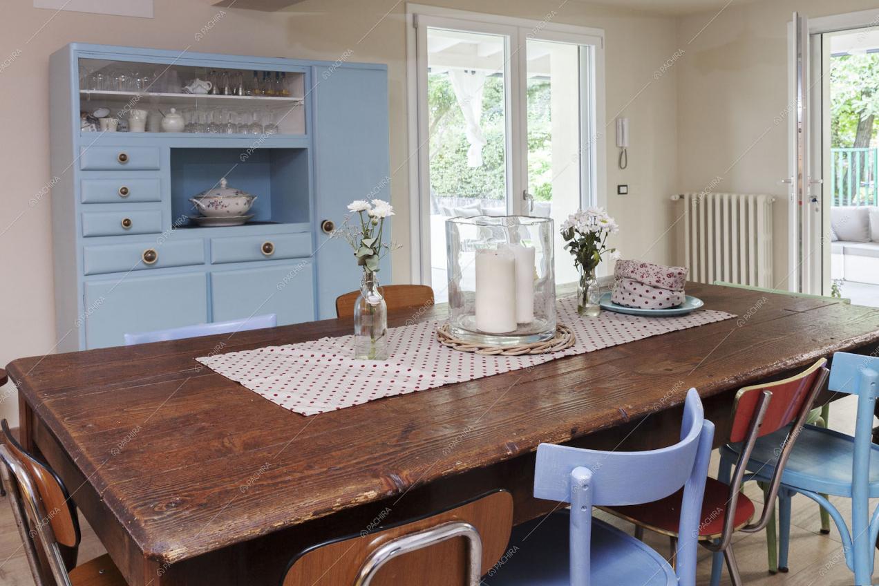 Tavolo da pranzo in legno, credenza azzurra e porte-finestre per accedere alla veranda