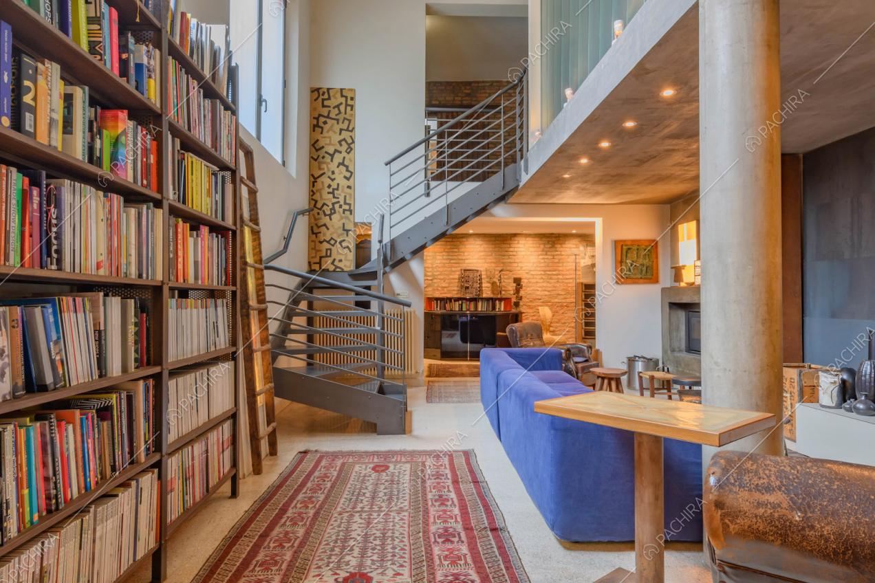 Libreria nella sala con colonna, scala in metallo e divano blu elettrico