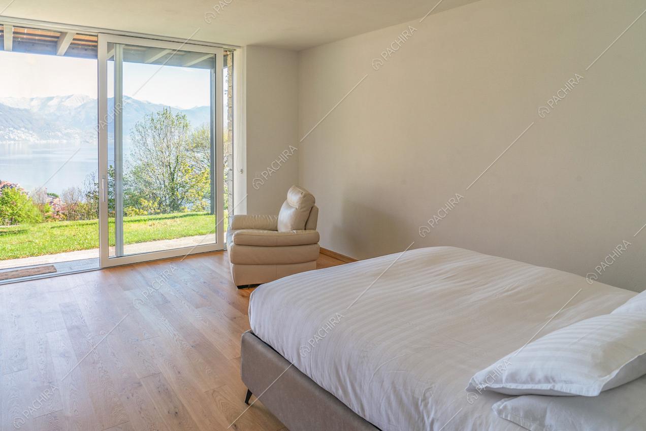 Letto matrimoniale in luminosa camera dalle pareti bianche con porta-finestra scorrevole