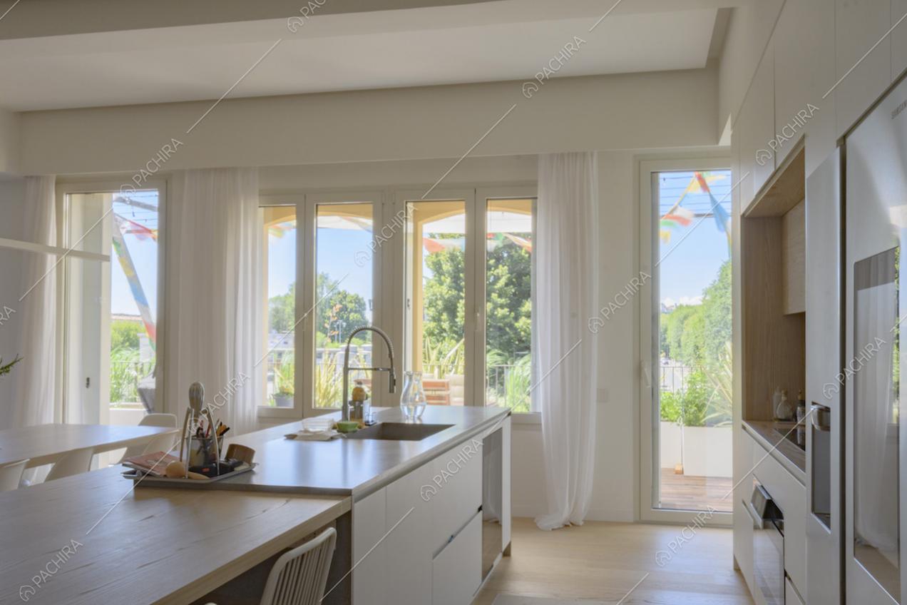 Cucina con mobili dai colori tenui e grandi finestre