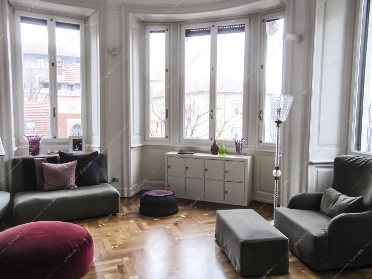 Soggiorno con divani e pouf, pavimento in parquet e ampie finestre che illuminano l'ambiente