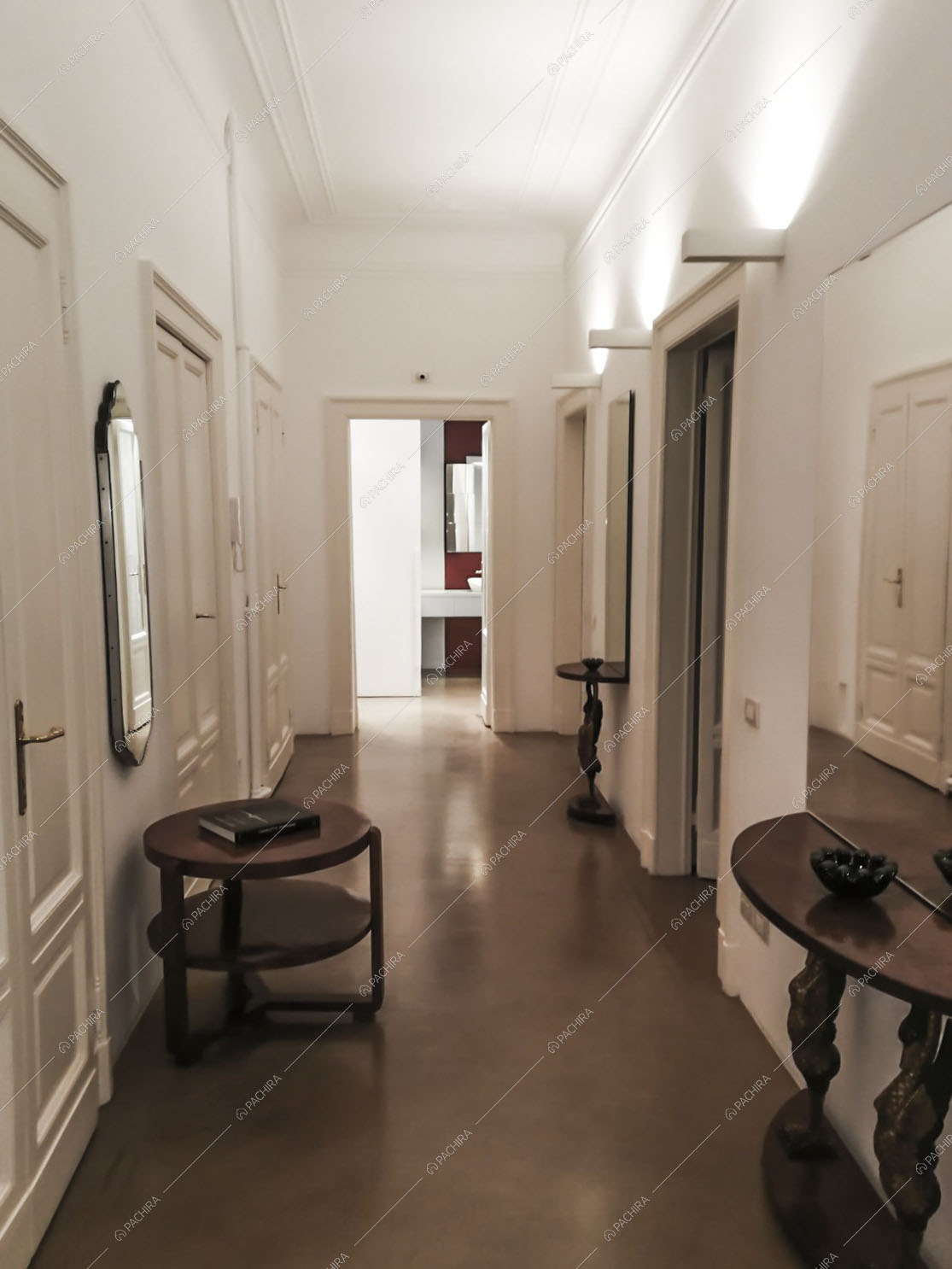 Corridoio con antichi tavolini in legno e soffitto e pareti bianchi con boiserie