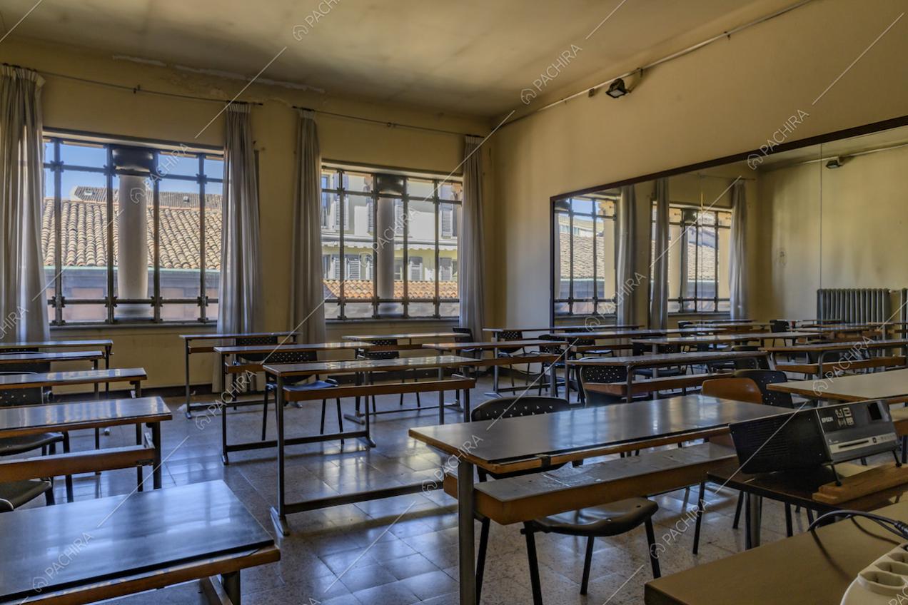 Ampia aula dalle pareti gialle, con specchio a parete, numerosi banchi e pavimento in piastrelle