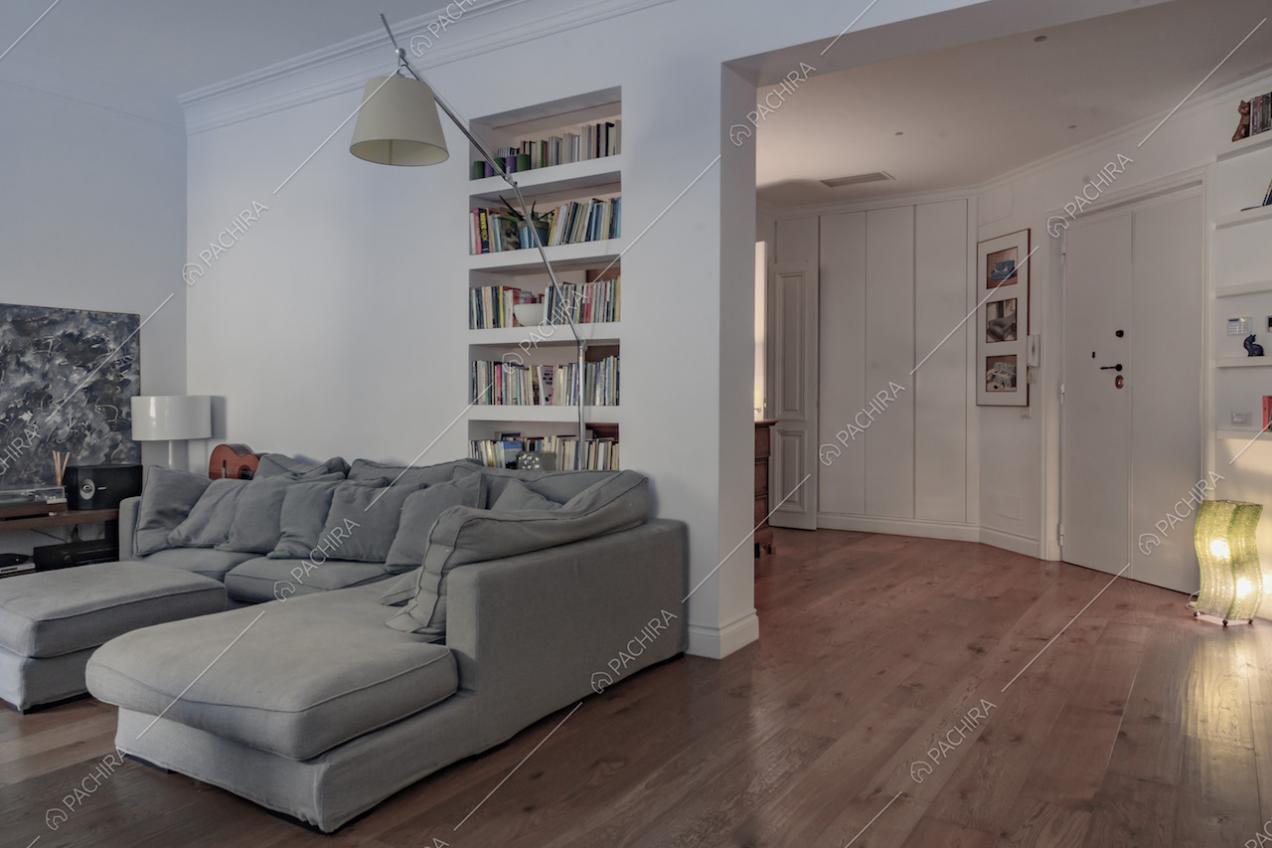 Vista sul divano grigio e sull'ingresso con pareti e soffitto bianchi con boiserie