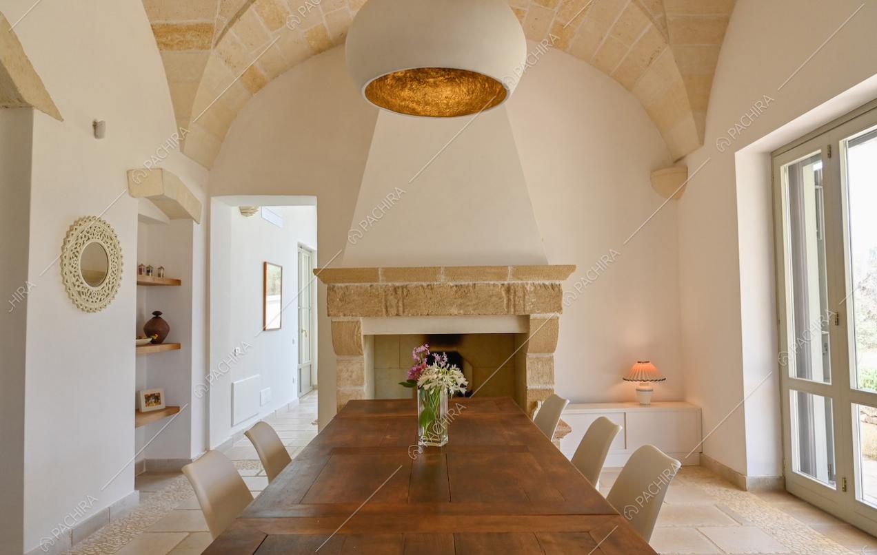 Ampia sala da pranzo dalle pareti bianche con tavolo in legno, camino e pavimento in pietra