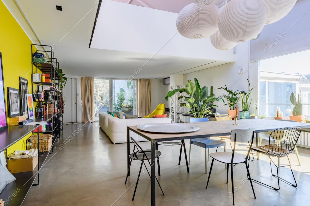 Tavolo da pranzo nella luminosa zona living con vetrate, parete gialla e vista sul parapetto del soppalco