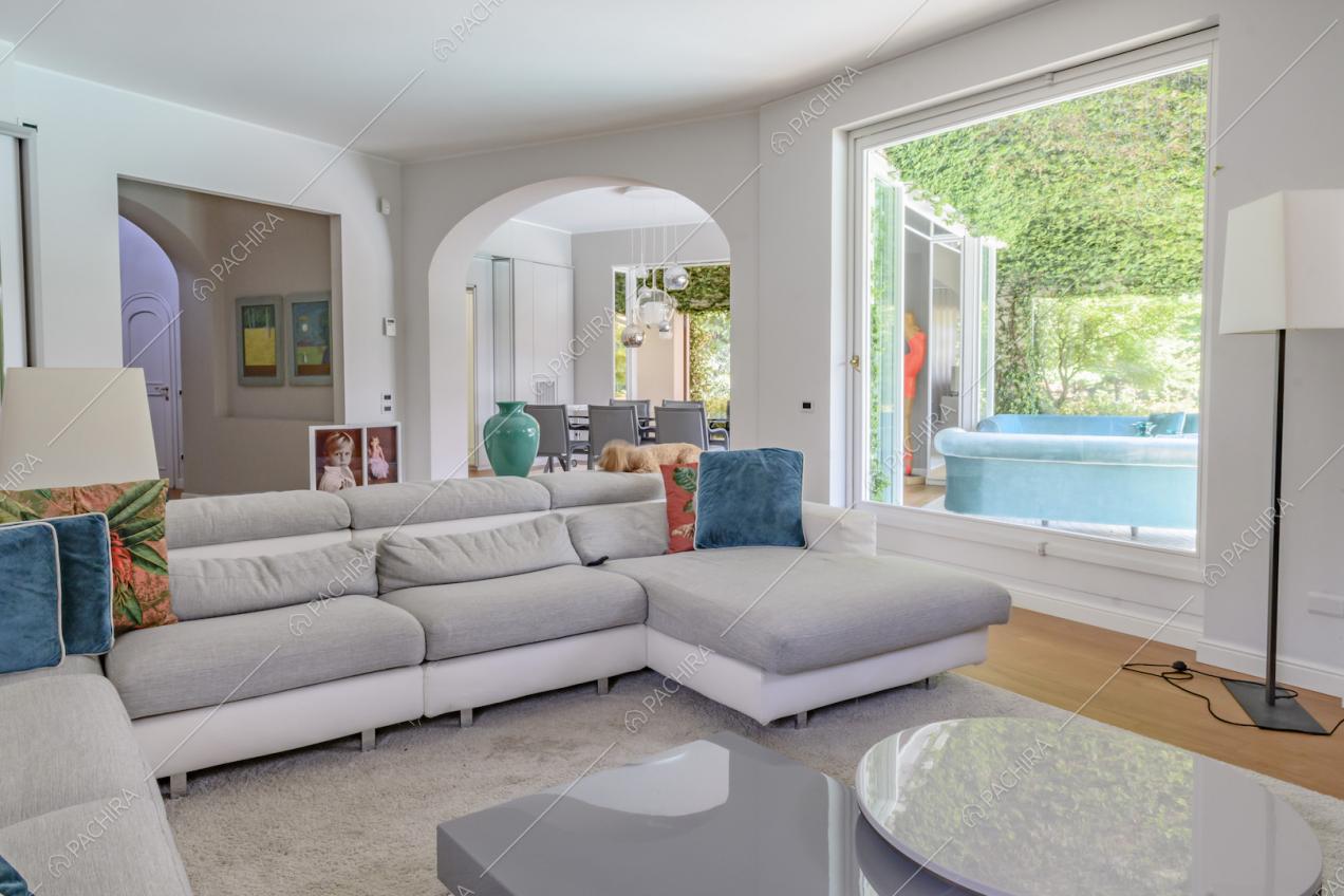Salotto con tavolino e divano bianco e grigio, pavimento in parquet e tramite un'ampia vetrata vista sulla veranda