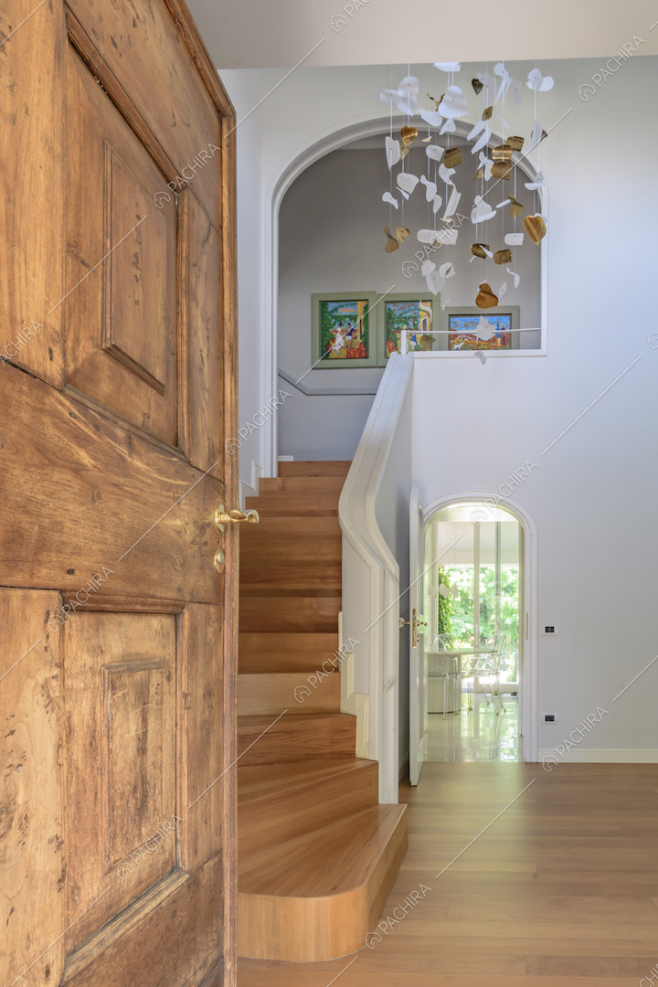 Porta in legno grezzo e atrio con pavimento in parquet, scala curva e pareti bianche