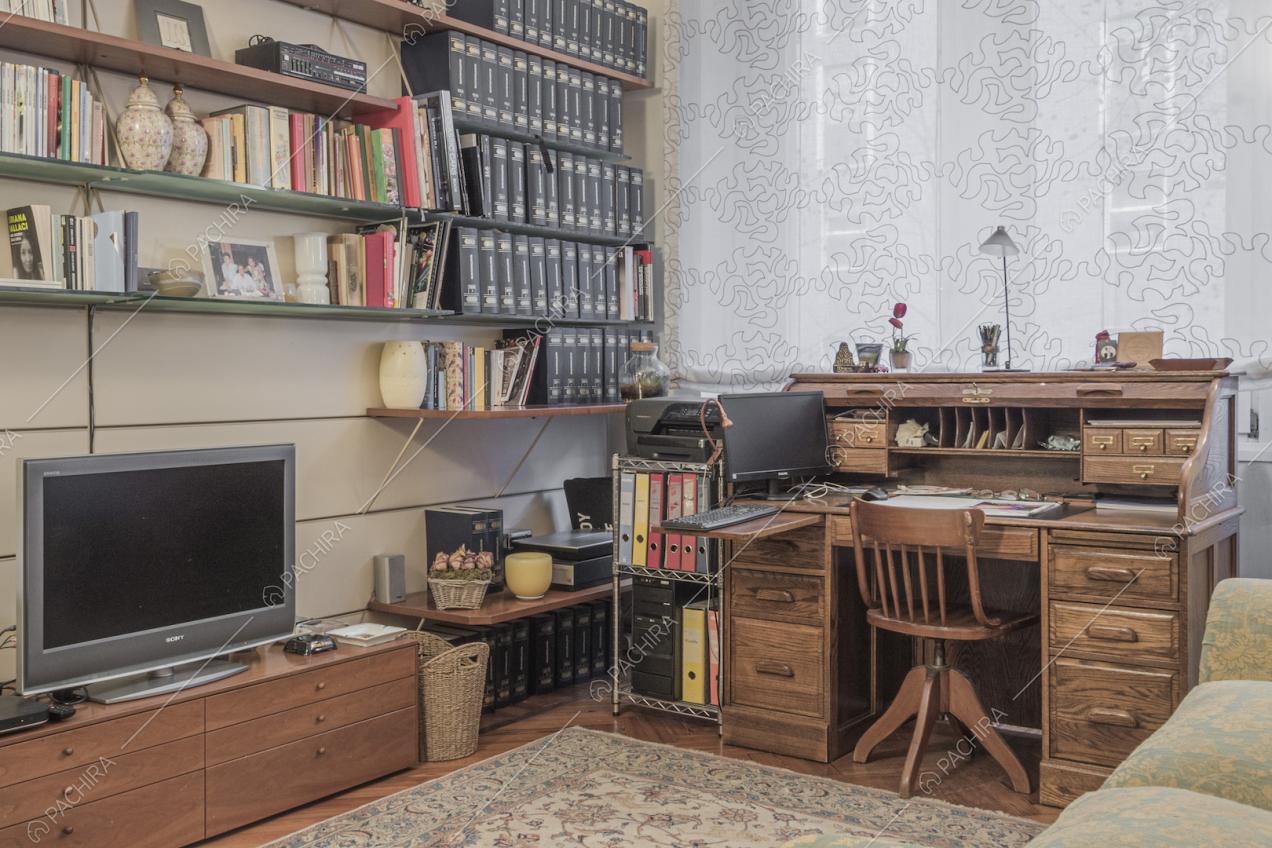 Studio con scrivania, mensole piene di libri e televisore