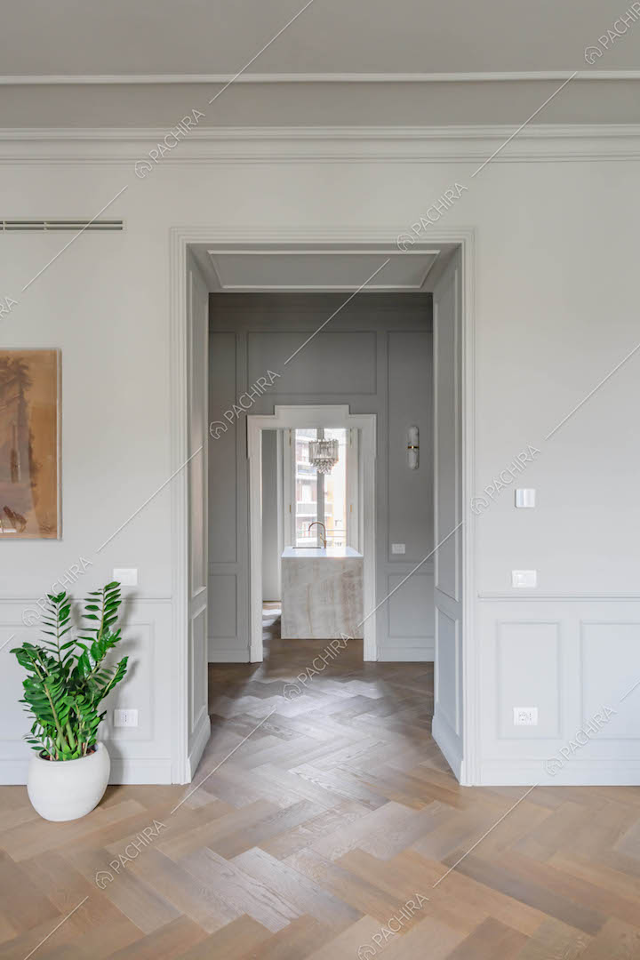 Luminosa sala con pavimento in parquet a spina di pesce, boiserie alle pareti e vista sulla cucina