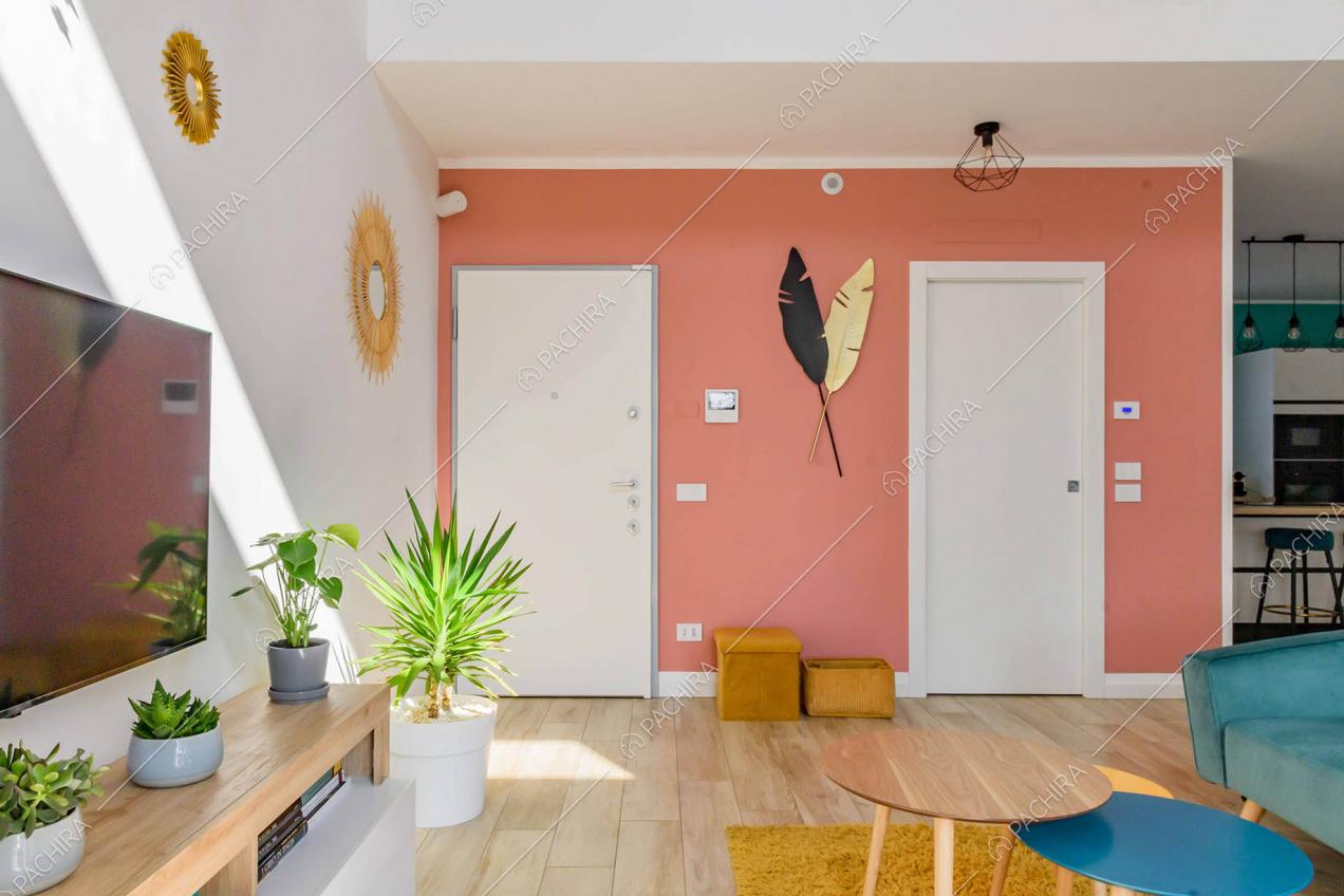 Salotto con tavolini in legno e vista sulla porta d'ingresso con parete rosa