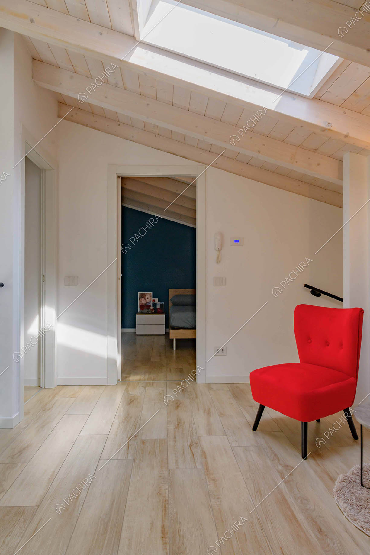 Poltrona rossa nell'atrio con lucernario, pavimento in parquet e vista sulla camera da letto matrimoniale