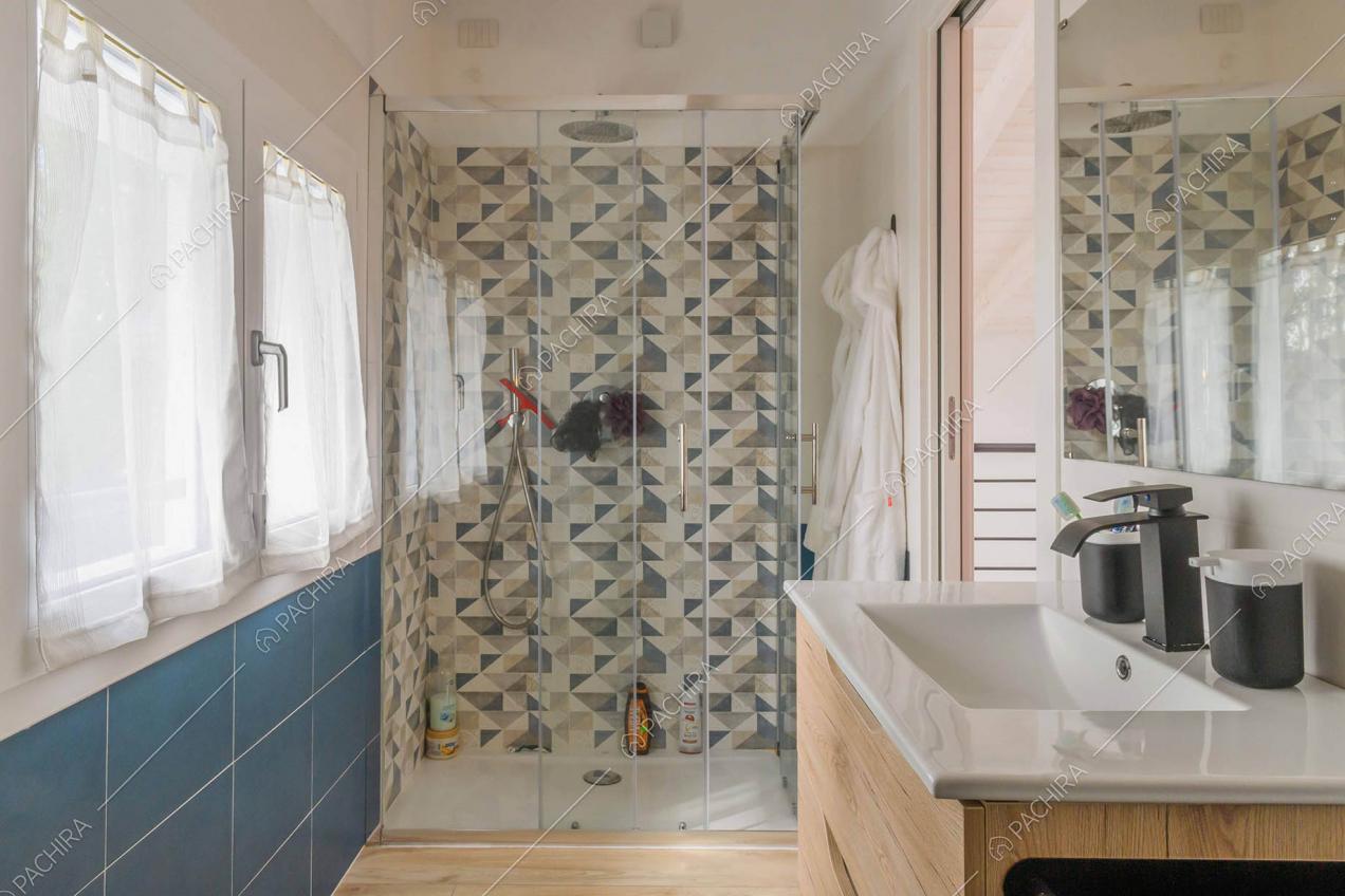 Bagno con parete in piastrelle blu, box doccia e pavimento in parquet