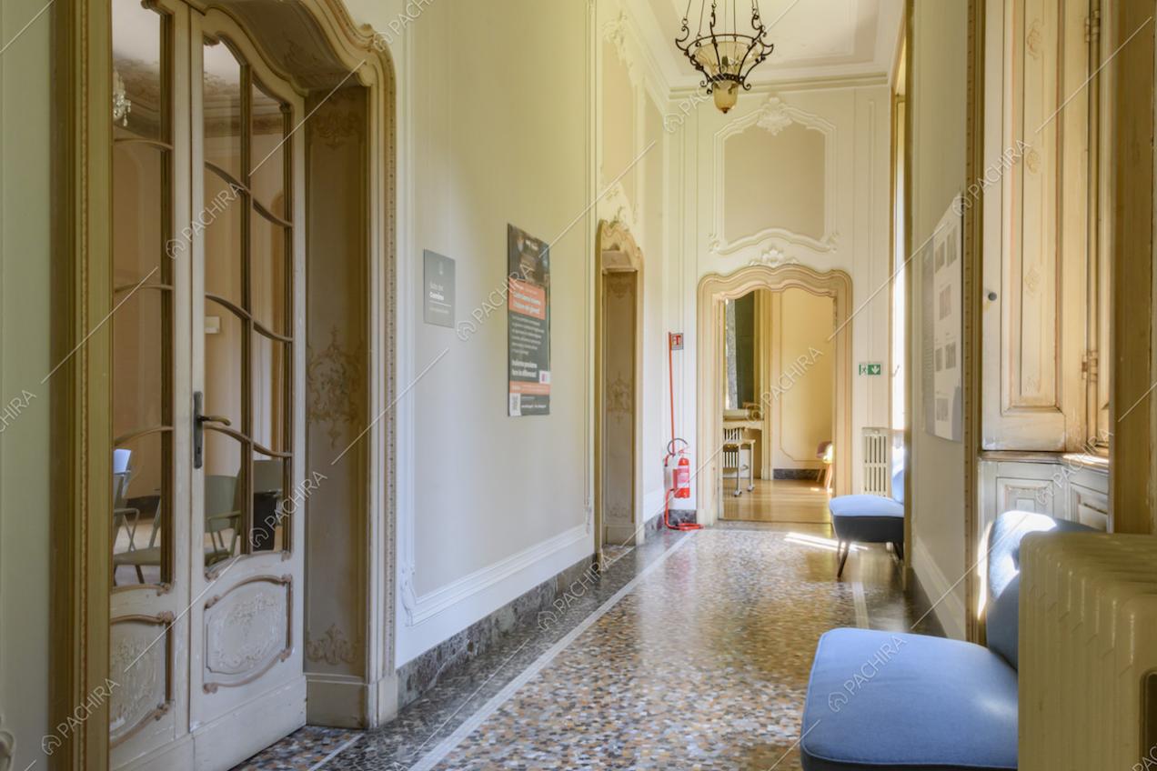 Luminoso corridoio con pavimento in graniglia, boiserie alle pareti e vista su un salone
