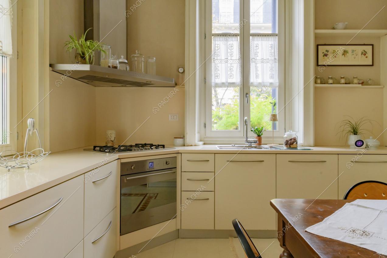 Luminosa cucina bianca a parete con fornelli a gas e tavolo da pranzo in legno