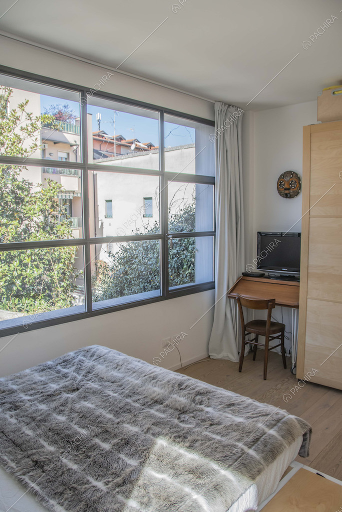 Camera da letto matrimoniale con finestra in stile industriale, scrivania e pavimento in parquet