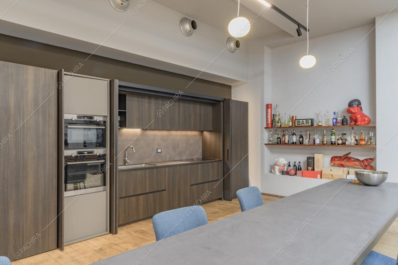 Dal tavolo da pranzo vista sulla cucina a muro in legno con fornelli a induzione