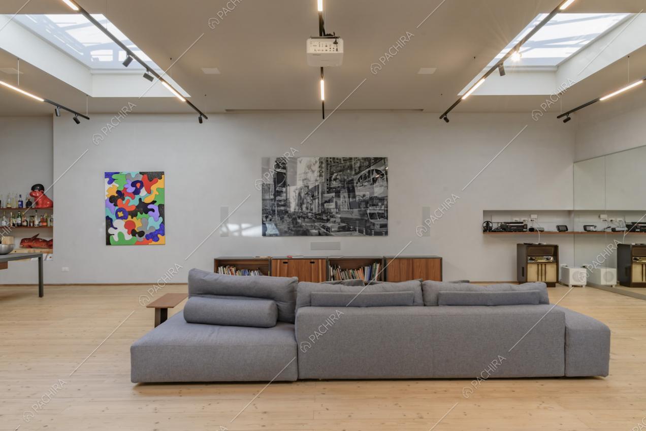 Divano grigio nell'ampia sala illuminata da lucernari e con pavimento in parquet