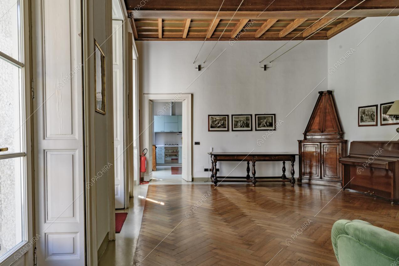 Ampia sala dalle pareti bianche e pavimento in parquet a spina di pesce si affaccia sulla cucina