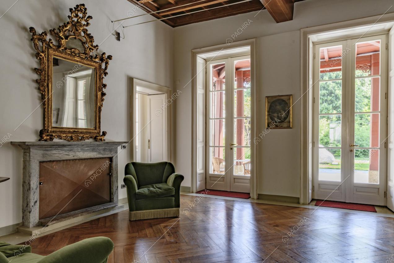 Dalla sala con pavimento in parquet a spina di pesce, pareti bianche e camino chiuso, accesso alla veranda tramite porte-finestre