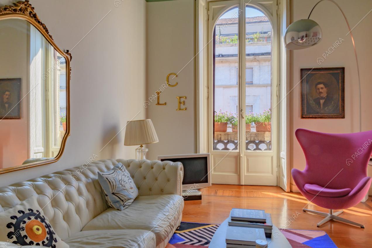 Nel salotto divano in pelle bianco, specchio con cornice dorata, poltrona fucsia e lampada di design