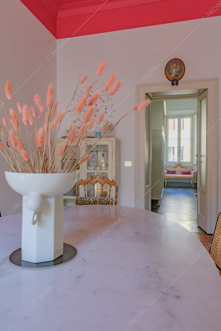 Tavolo da pranzo in marmo con vaso da fiori, pareti bianche e soffitto fucsia con boiserie