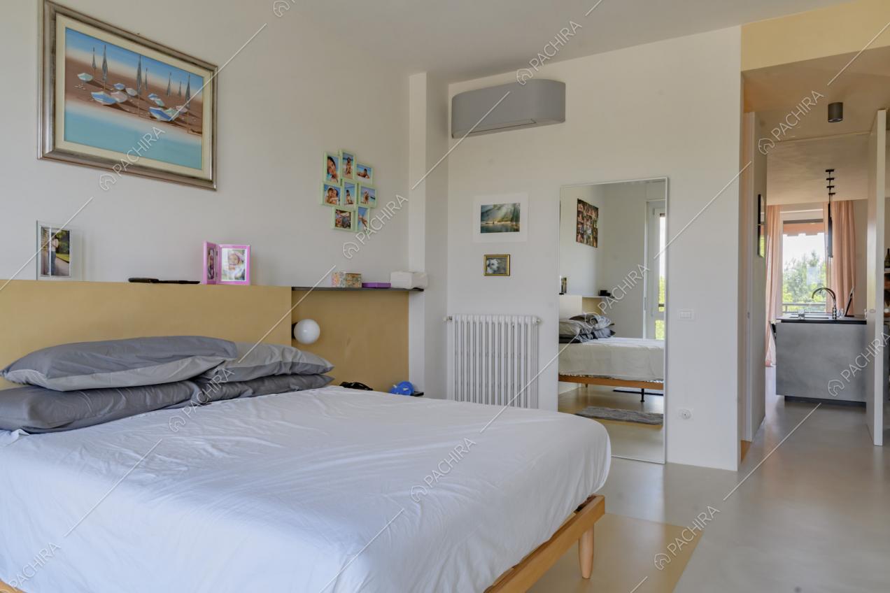 Camera da letto matrimoniale con pavimento in cemento lisciato bianco e vista sull'isola della cucina