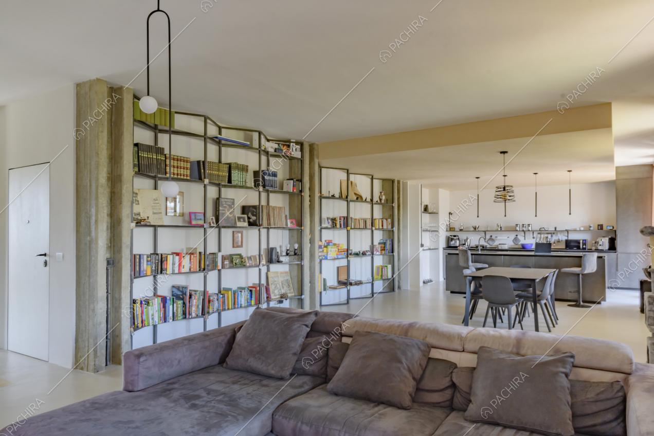 Divano marrone nella zona living con libreria di design e vista sulla cucina a isola