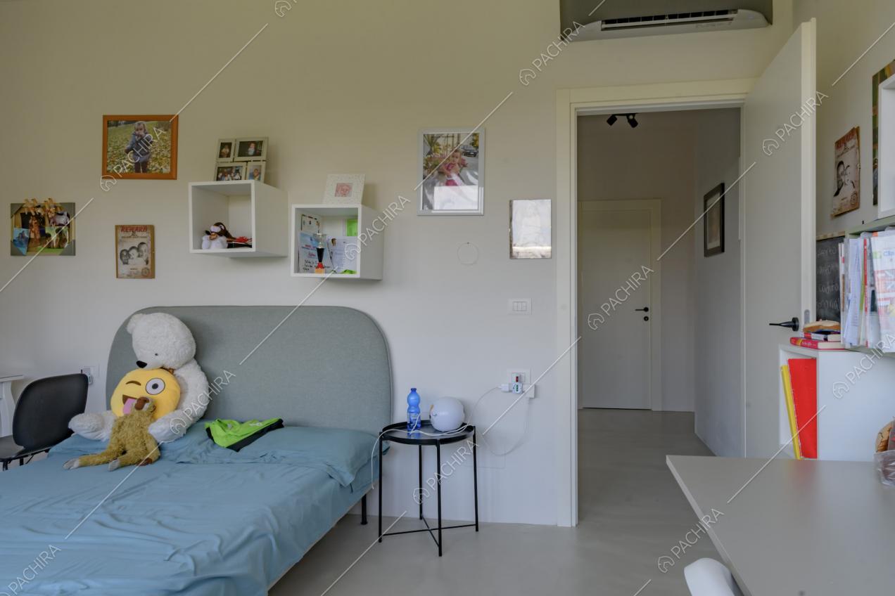Camera da letto con pavimento in cemento lisciato, scrivania e pareti bianche