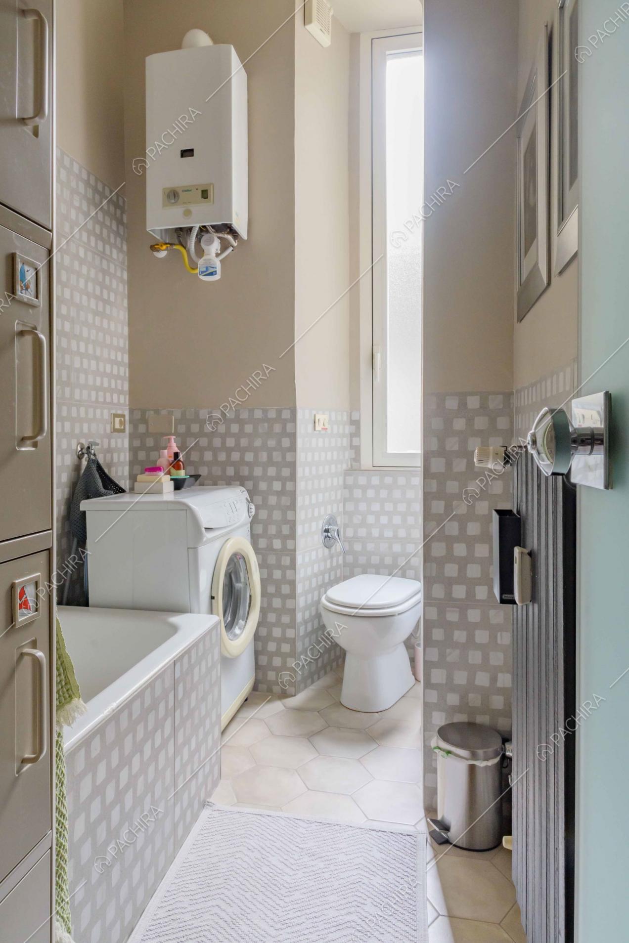 Bagno con vasca, pareti con fantasia grigia e bianca e pavimento in cementine