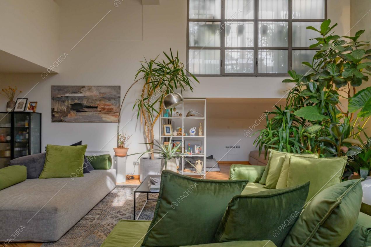 Salotto con grandi finestre in stile industriale, pouf grigio e divano verde angolare