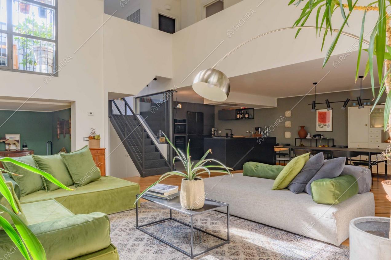 Luminoso salotto con divano verde angolare, pouf grigio e vista sulle scale e sul soppalco