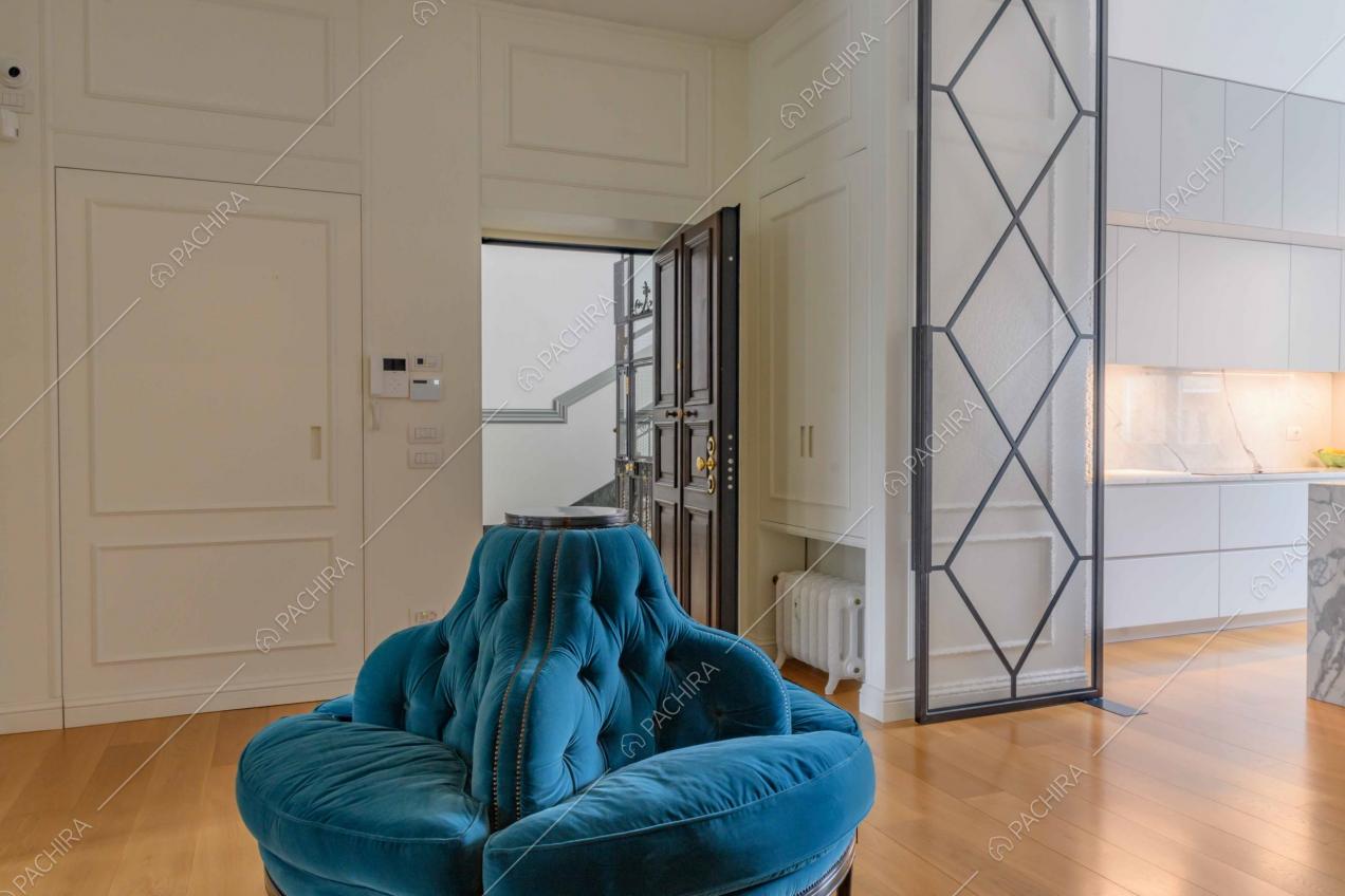 Poltrona di velluto blu nell'atrio e vista sulla cucina con pavimento in parquet