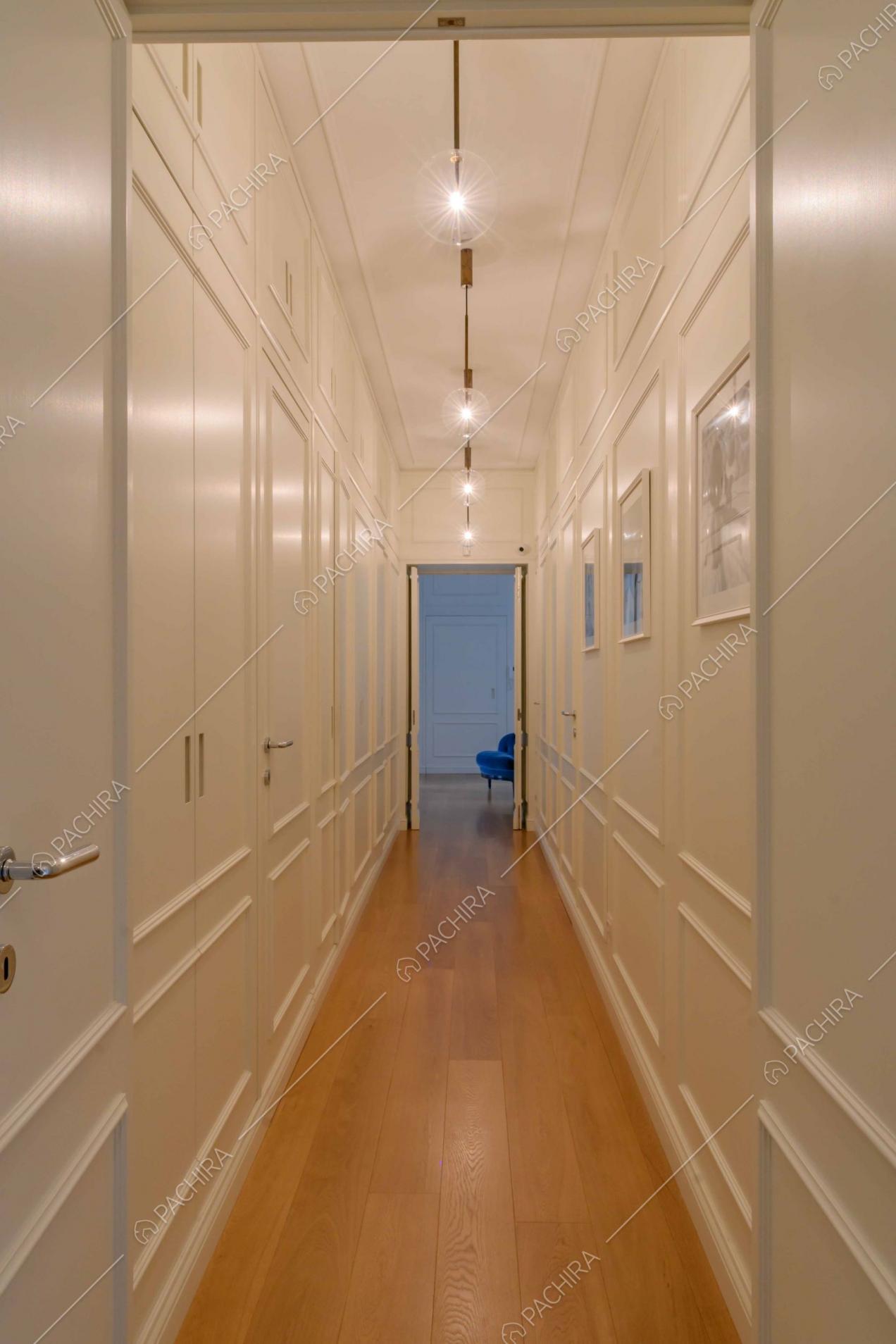 Dal lungo corridoio con pavimento in parquet vista sulla poltrona blu di velluto