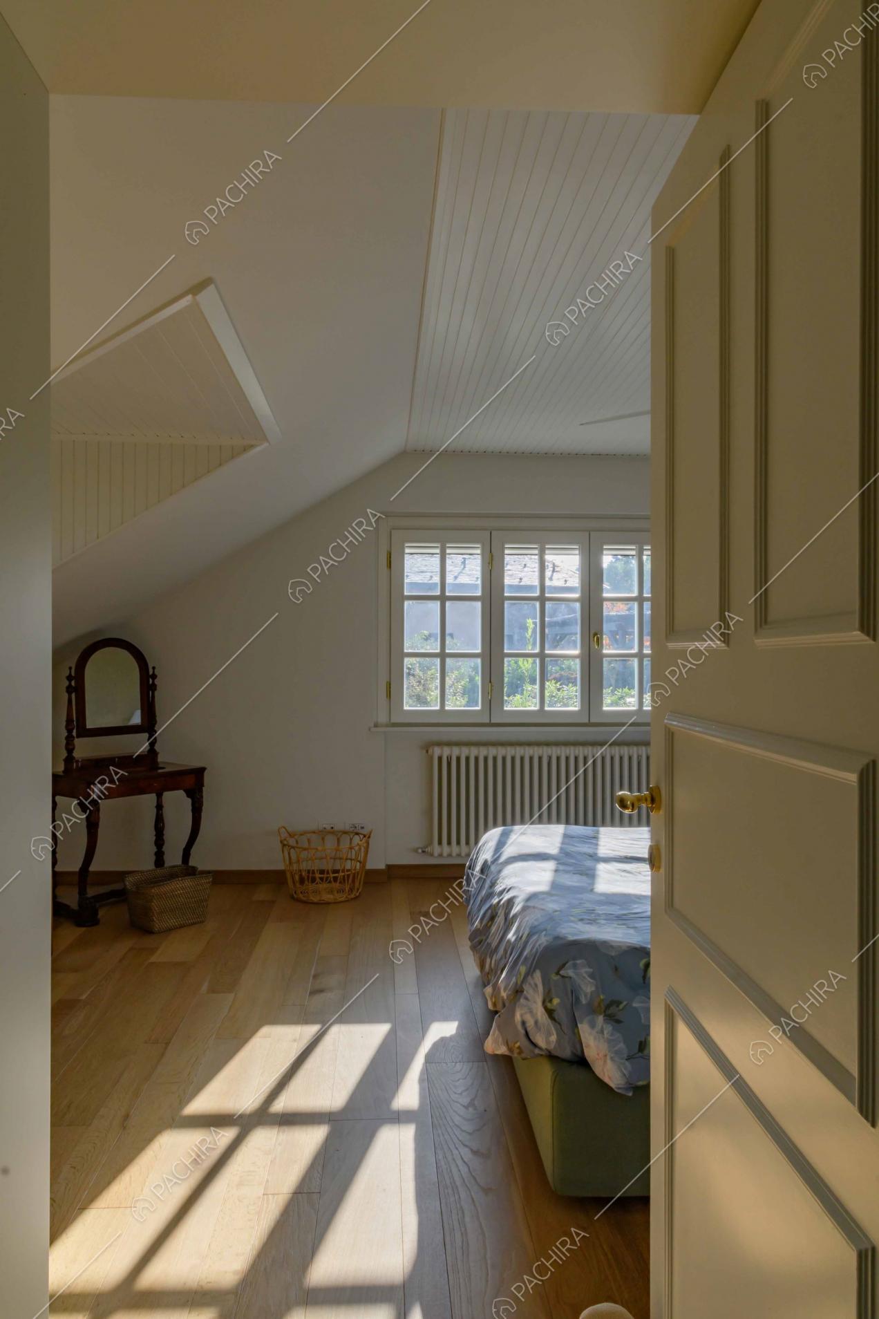 Letto matrimoniale nella luminosa camera con pavimento in parquet e pareti bianche